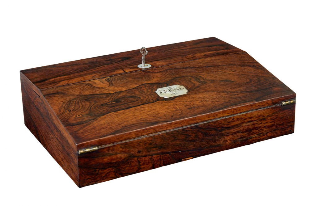 A 19th-century William IV figured rosewood writing slope featuring a slanted top, metal key, and an inlaid plaque dated 1835.