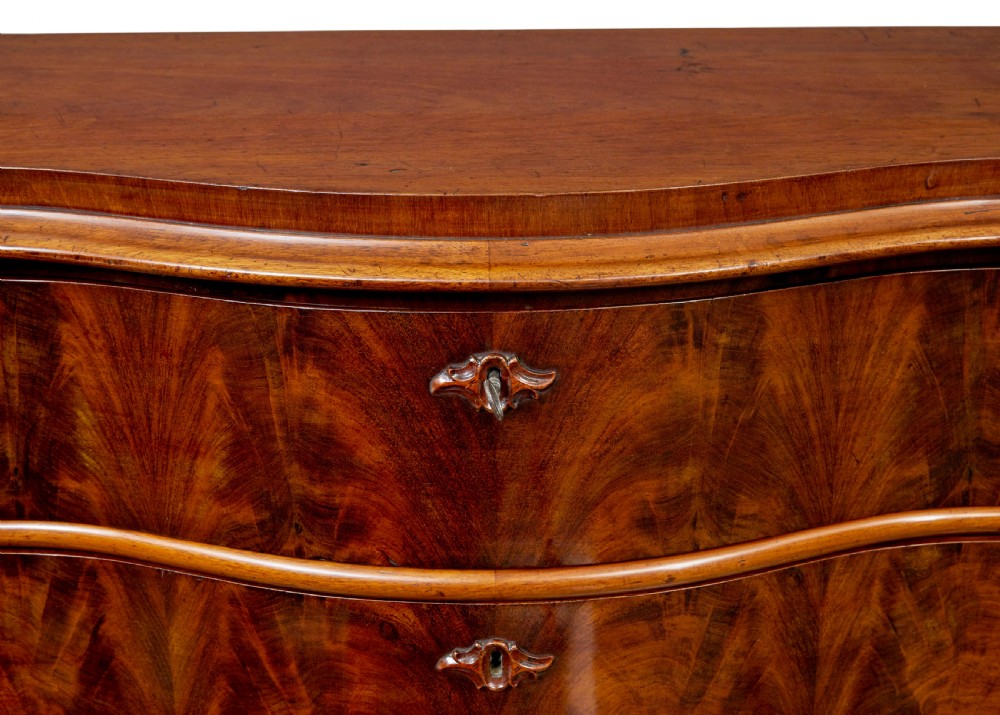 A 19th-century Swedish mahogany chest of drawers with a serpentine front, four drawers, flame timber veneer, carved side accents, and turned feet. View VIII