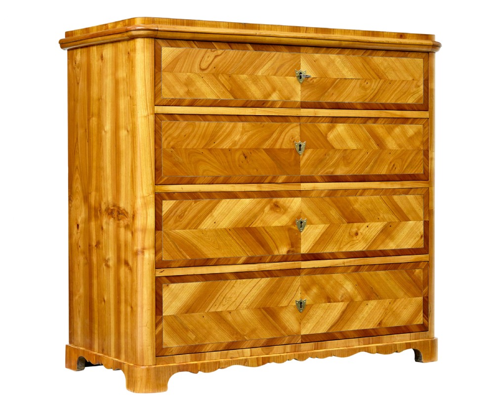 A mid-nineteenth-century Scandinavian chest of drawers crafted from inlaid elm wood with chevron patterns across four drawers and brass shield keyhole escutcheons.