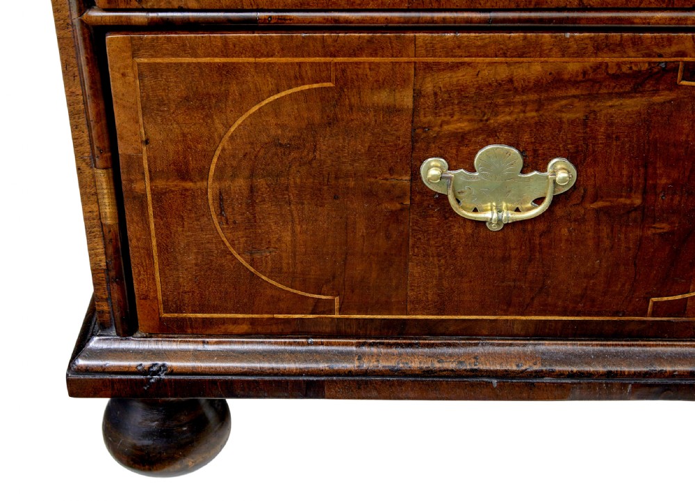 A 17th-century William and Mary walnut chest of drawers with decorative line inlay, brass drop handles, and turned bun feet. View IX
