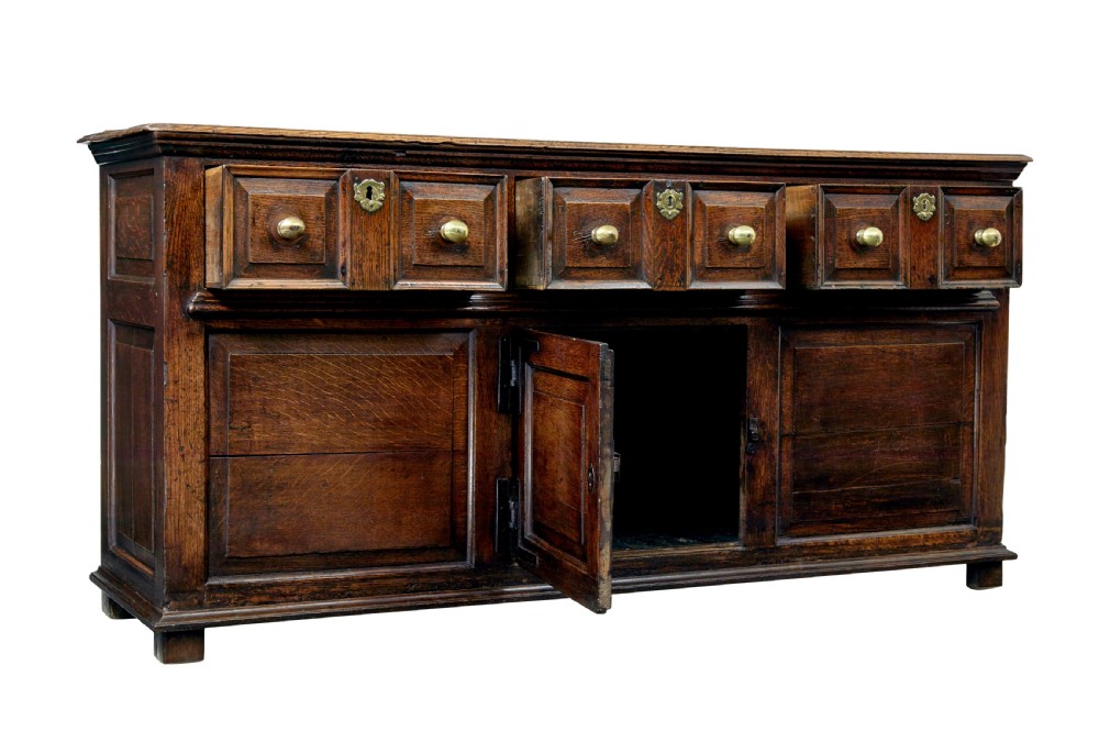 An 18th-century dark oak dresser featuring three geometric panelled drawers with brass knobs above cupboard doors with iron hinges. View II