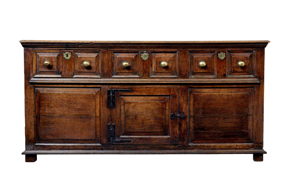An 18th-century dark oak dresser featuring three geometric panelled drawers with brass knobs above cupboard doors with iron hinges. View III
