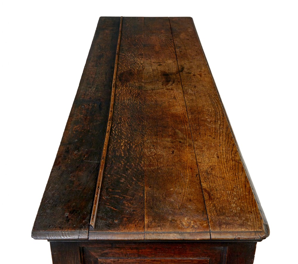An 18th-century dark oak dresser featuring three geometric panelled drawers with brass knobs above cupboard doors with iron hinges. View XI