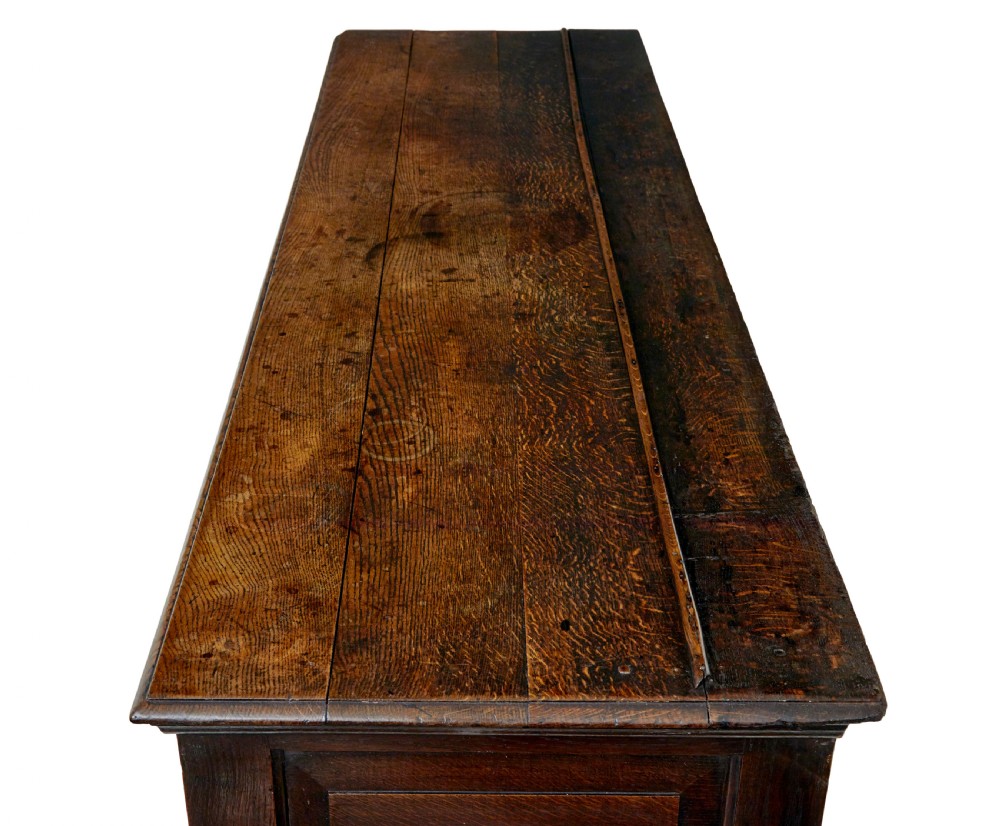 An 18th-century dark oak dresser featuring three geometric panelled drawers with brass knobs above cupboard doors with iron hinges. View XII