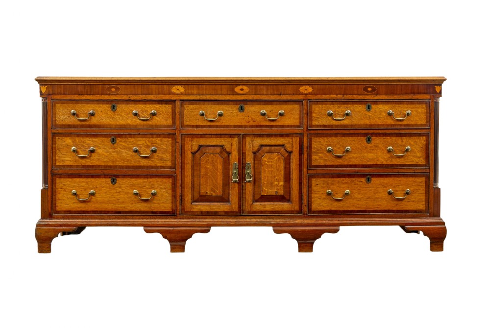 An 18th-century inlaid oak Lancashire dresser base featuring six drawers, a central two-door fielded panel cupboard, brass handles, and ogee bracket feet. View II