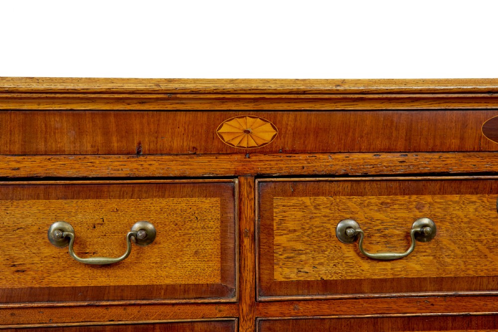 An 18th-century inlaid oak Lancashire dresser base featuring six drawers, a central two-door fielded panel cupboard, brass handles, and ogee bracket feet. View X