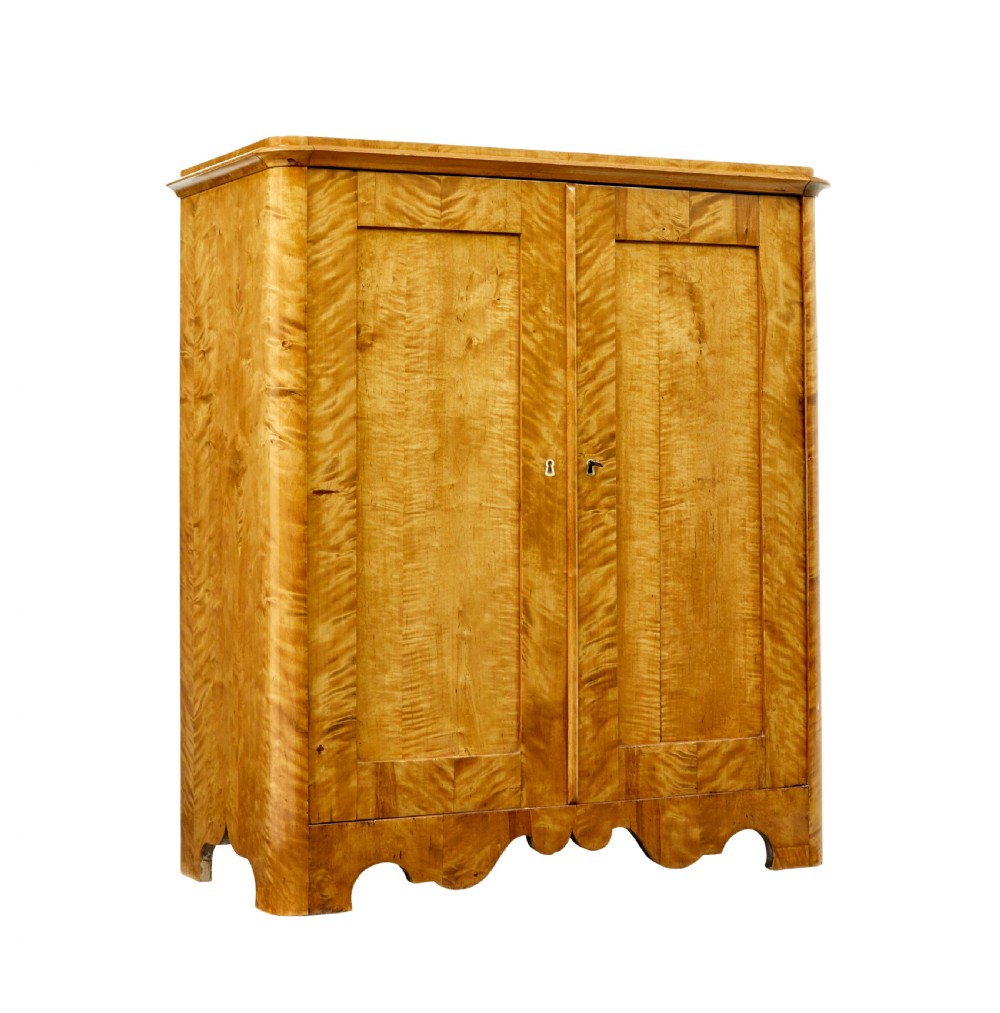 A nineteenth-century Swedish satin birch cupboard featuring two panelled doors with keyhole escutcheons and a shaped scalloped apron base.