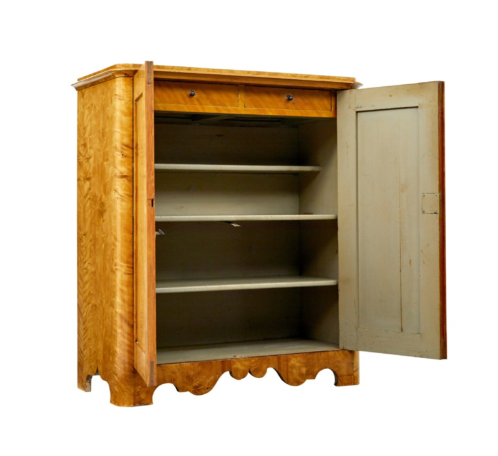 A nineteenth-century Swedish satin birch cupboard featuring two panelled doors with keyhole escutcheons and a shaped scalloped apron base. View II