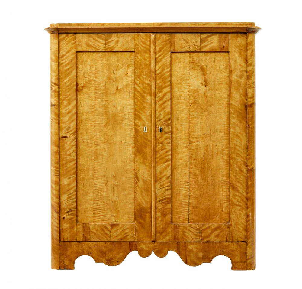 A nineteenth-century Swedish satin birch cupboard featuring two panelled doors with keyhole escutcheons and a shaped scalloped apron base. View IV