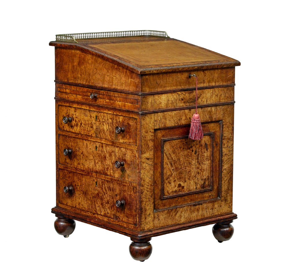A mid-nineteenth century pollard oak Davenport desk featuring a sloped leather writing top with a brass gallery rail, side drawers with wooden knobs, and turned feet.