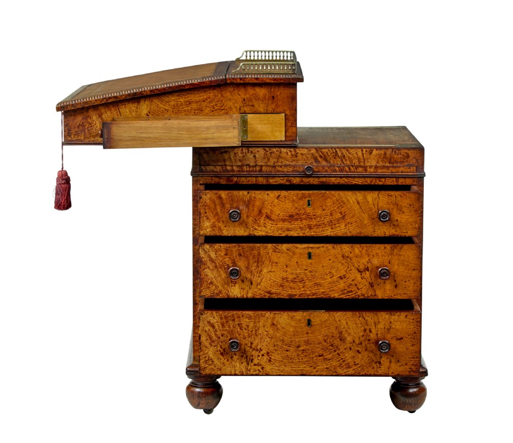 A mid-nineteenth century pollard oak Davenport desk featuring a sloped leather writing top with a brass gallery rail, side drawers with wooden knobs, and turned feet. View V