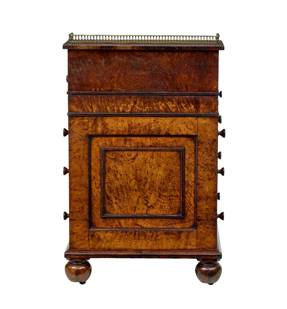 A mid-nineteenth century pollard oak Davenport desk featuring a sloped leather writing top with a brass gallery rail, side drawers with wooden knobs, and turned feet. View VI
