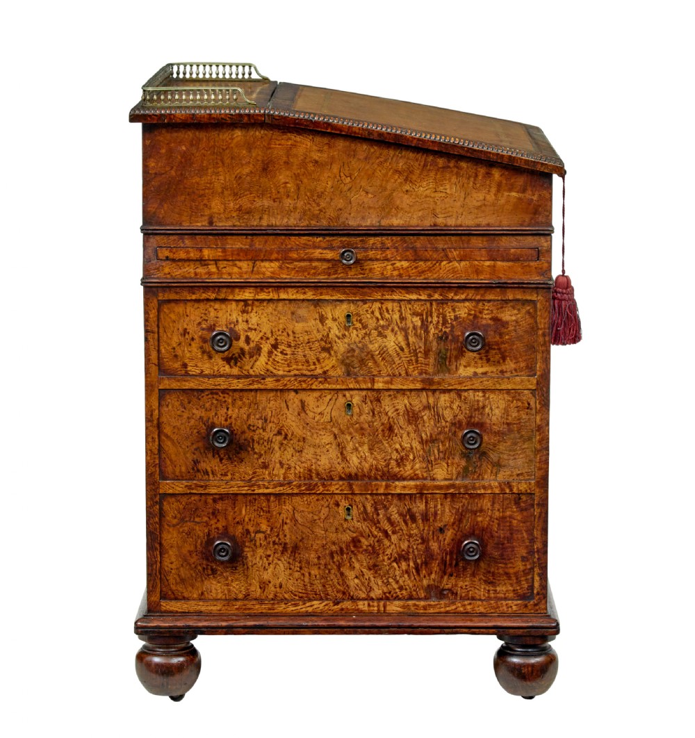 A mid-nineteenth century pollard oak Davenport desk featuring a sloped leather writing top with a brass gallery rail, side drawers with wooden knobs, and turned feet. View VII