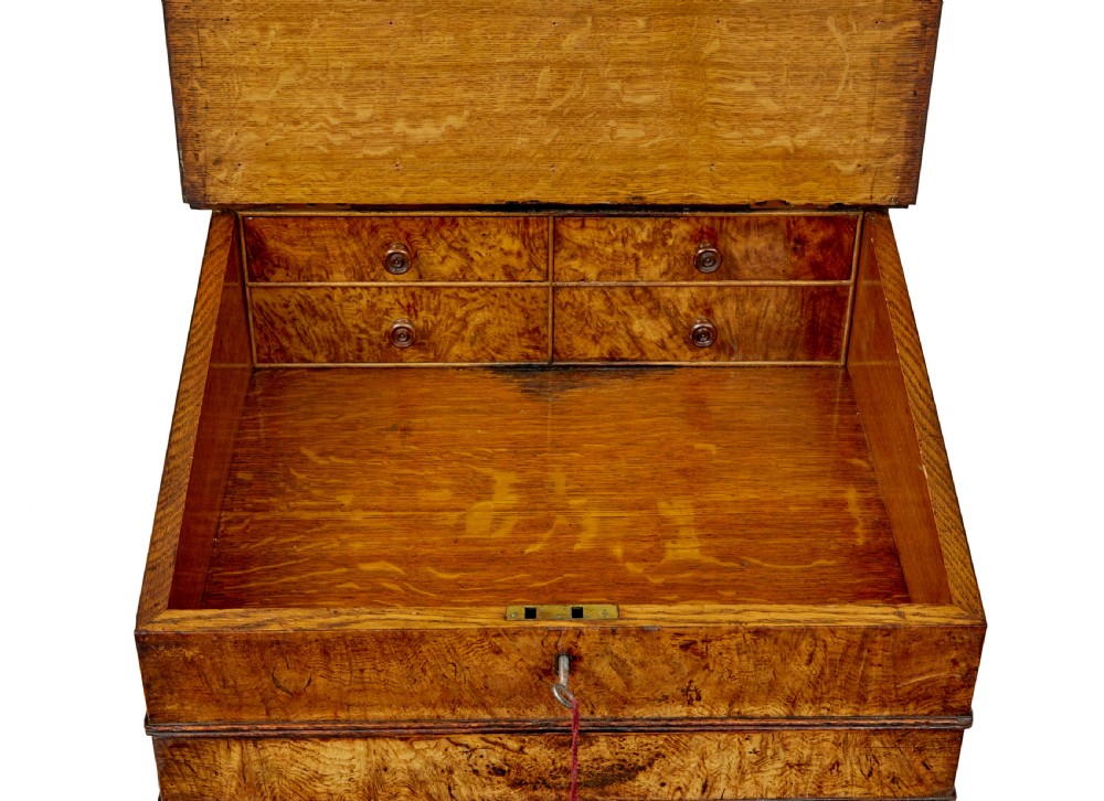 A mid-nineteenth century pollard oak Davenport desk featuring a sloped leather writing top with a brass gallery rail, side drawers with wooden knobs, and turned feet. View IX