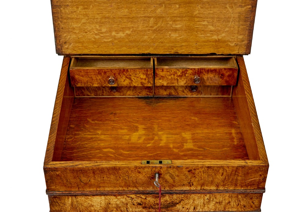 A mid-nineteenth century pollard oak Davenport desk featuring a sloped leather writing top with a brass gallery rail, side drawers with wooden knobs, and turned feet. View X