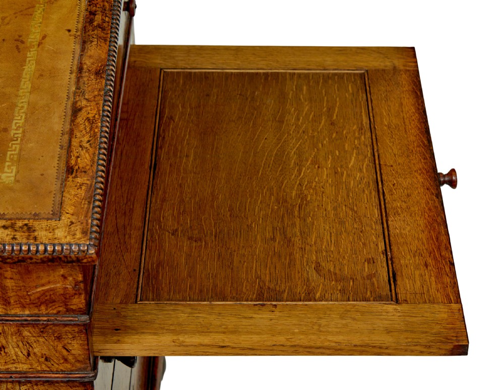 A mid-nineteenth century pollard oak Davenport desk featuring a sloped leather writing top with a brass gallery rail, side drawers with wooden knobs, and turned feet. View XII