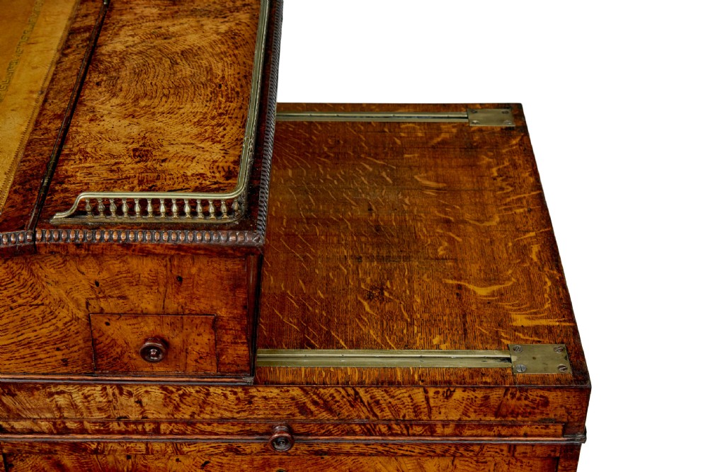 A mid-nineteenth century pollard oak Davenport desk featuring a sloped leather writing top with a brass gallery rail, side drawers with wooden knobs, and turned feet. View XIV