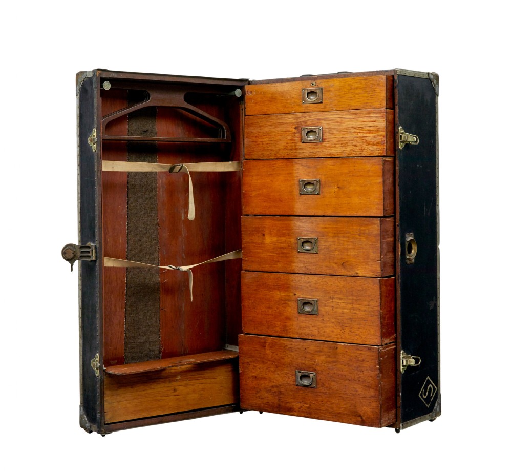 An open early 20th-century vertical steamer chest featuring a clothes hanging compartment with straps on the left and a column of six wooden drawers with recessed brass handles on the right. View II