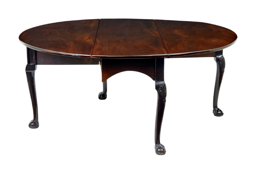 An eighteenth-century dark mahogany oval drop-leaf dining table featuring cabriole legs with carved knees and claw-and-ball feet.