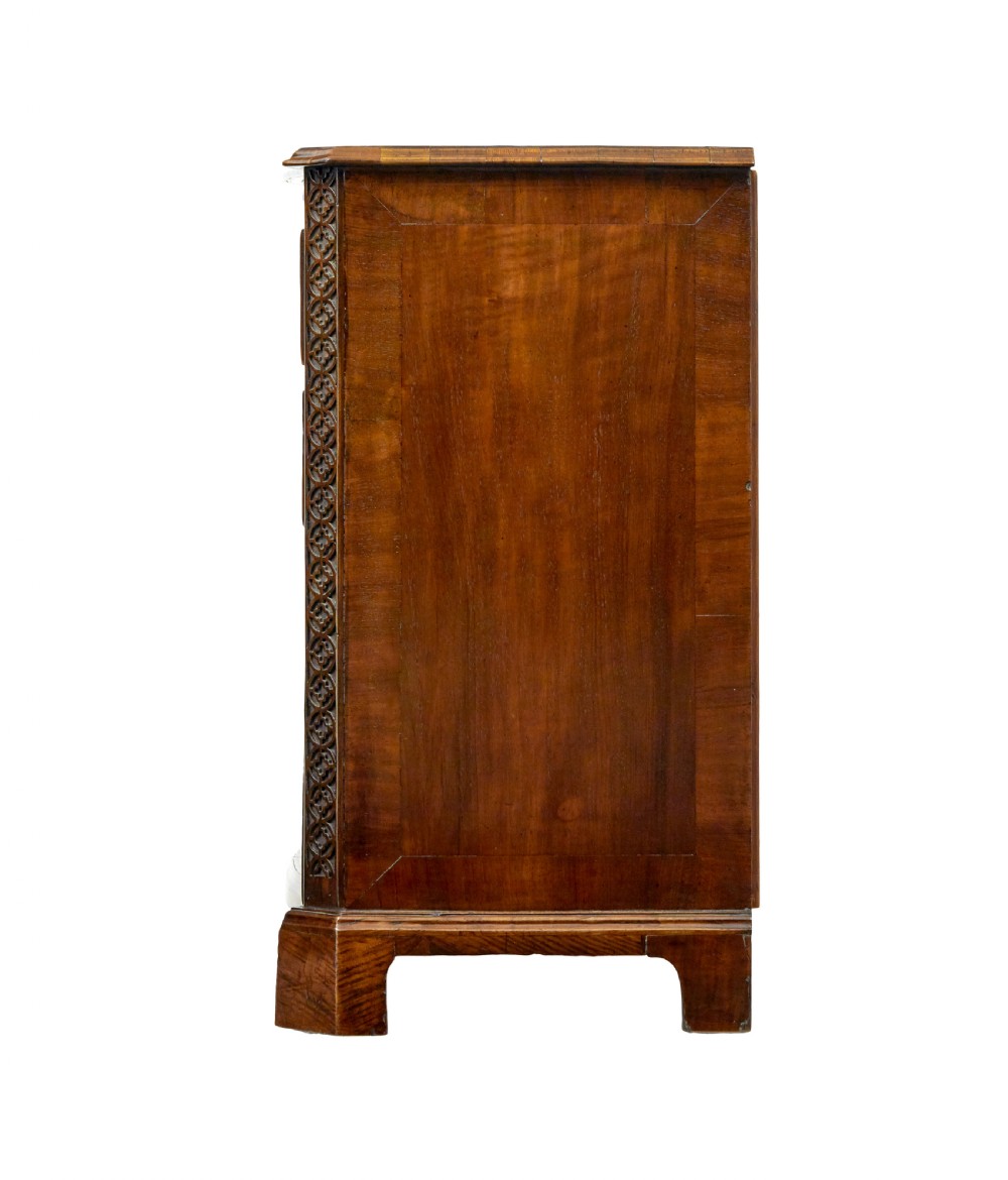 An early 19th-century walnut chest of drawers featuring four graduating drawers with brass handles, carved fretwork corners, and bracket feet. View V