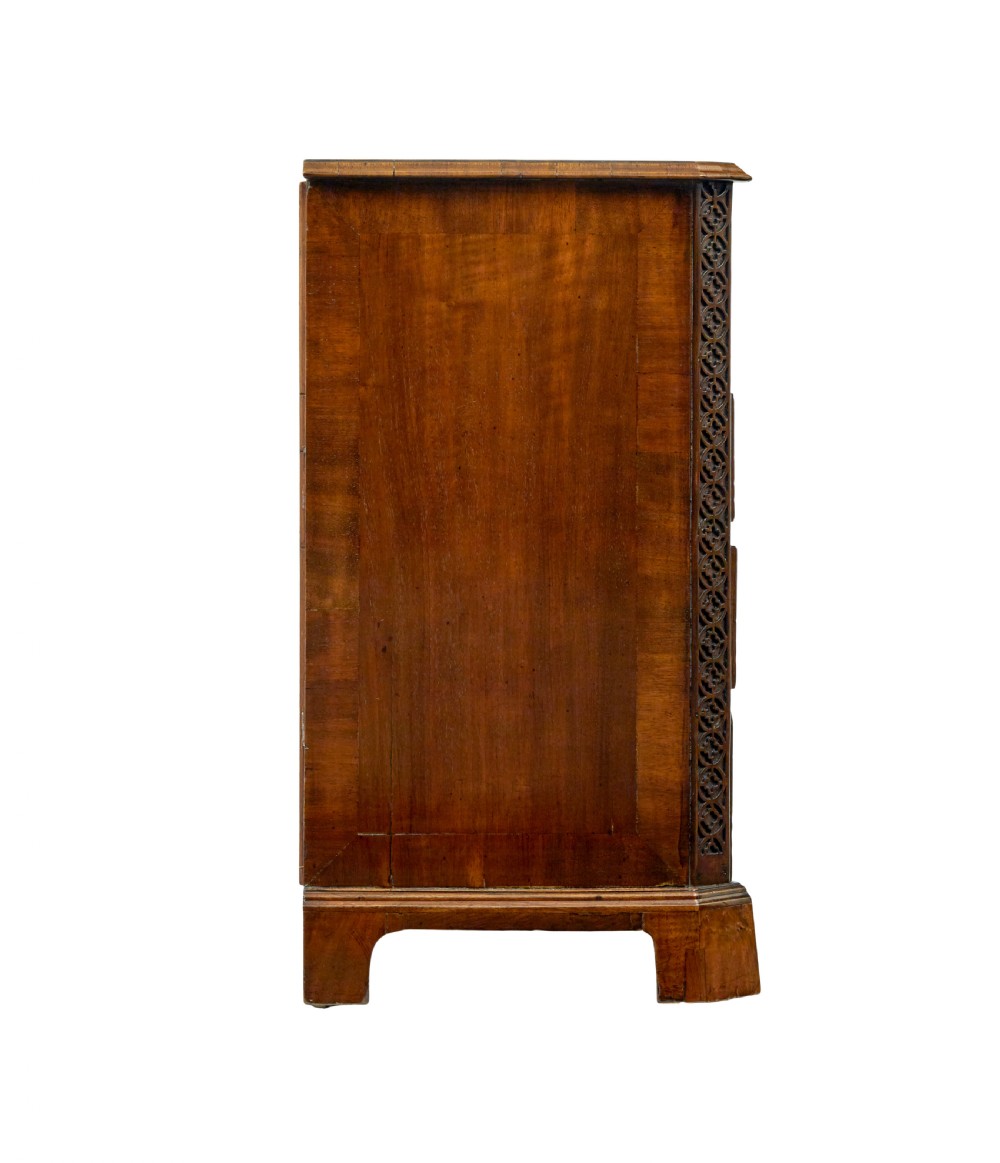 An early 19th-century walnut chest of drawers featuring four graduating drawers with brass handles, carved fretwork corners, and bracket feet. View VI