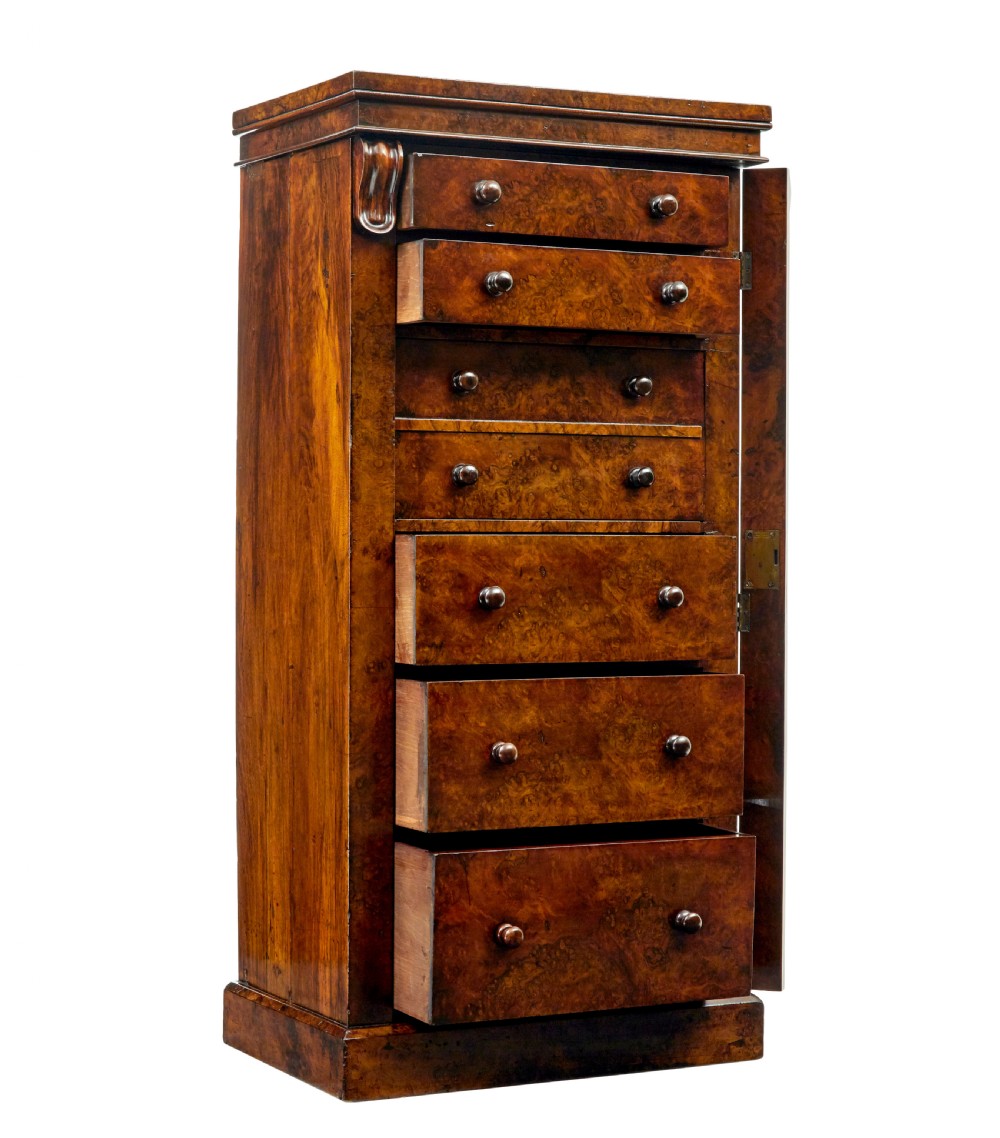 A tall, narrow Victorian burr walnut Wellington chest featuring seven graduated drawers with turned knob handles, decorative scroll brackets, and a locking side pilaster set upon a plinth base. View III