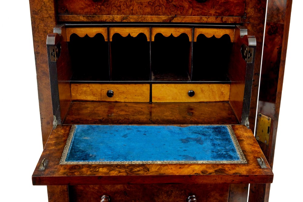 A tall, narrow Victorian burr walnut Wellington chest featuring seven graduated drawers with turned knob handles, decorative scroll brackets, and a locking side pilaster set upon a plinth base. View IX