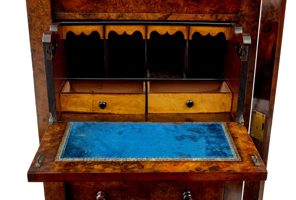 A tall, narrow Victorian burr walnut Wellington chest featuring seven graduated drawers with turned knob handles, decorative scroll brackets, and a locking side pilaster set upon a plinth base. View X