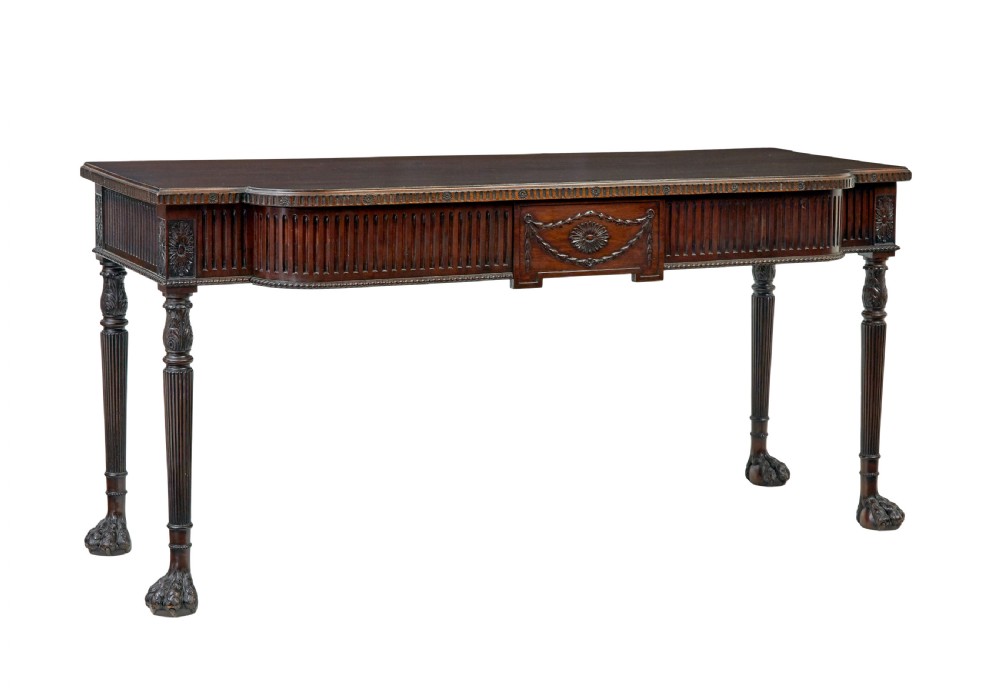 A nineteenth-century dark mahogany Irish serving table featuring a reeded frieze, central drawer with carved swag motif, and fluted legs with carved feet.