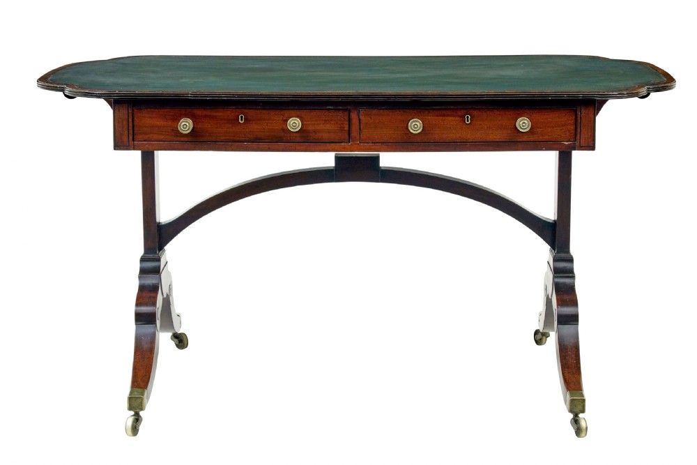 An early Victorian mahogany writing table featuring a green leather top, two drawers, an arched stretcher, and legs on brass castors.