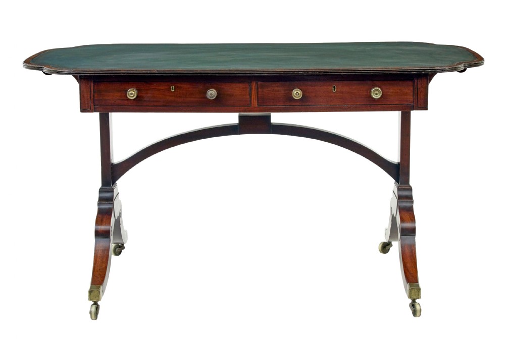An early Victorian mahogany writing table featuring a green leather top, two drawers, an arched stretcher, and legs on brass castors. View IV