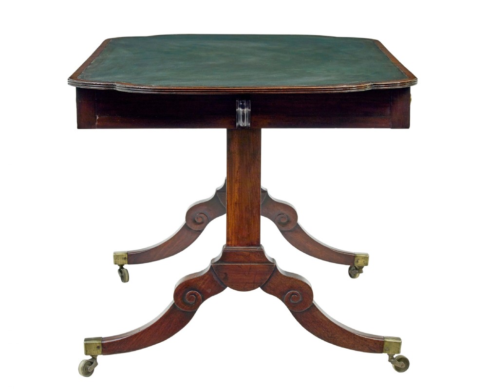 An early Victorian mahogany writing table featuring a green leather top, two drawers, an arched stretcher, and legs on brass castors. View V