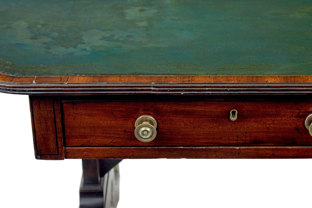 An early Victorian mahogany writing table featuring a green leather top, two drawers, an arched stretcher, and legs on brass castors. View VI