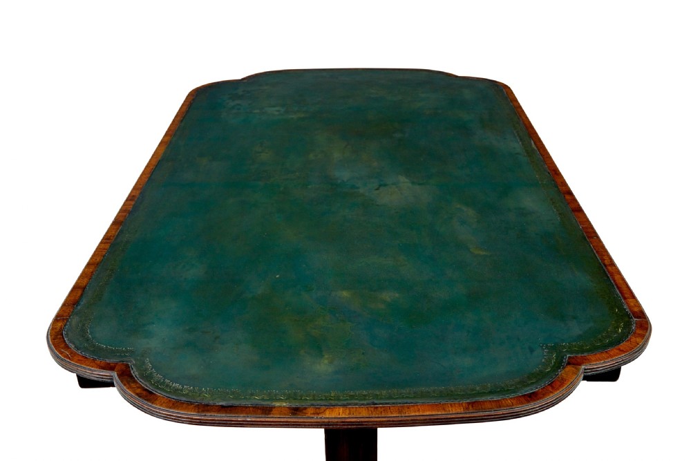 An early Victorian mahogany writing table featuring a green leather top, two drawers, an arched stretcher, and legs on brass castors. View VII