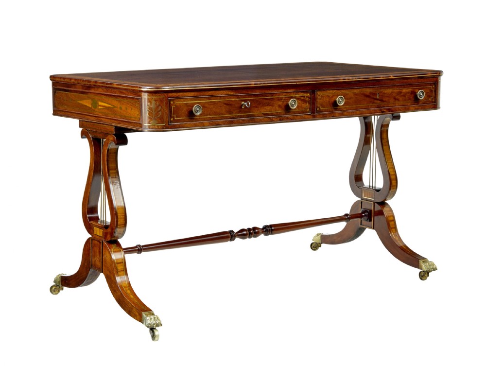 A 19th-century Regency writing desk featuring brass inlay, two frieze drawers, lyre-shaped end supports, and brass paw feet on castors.