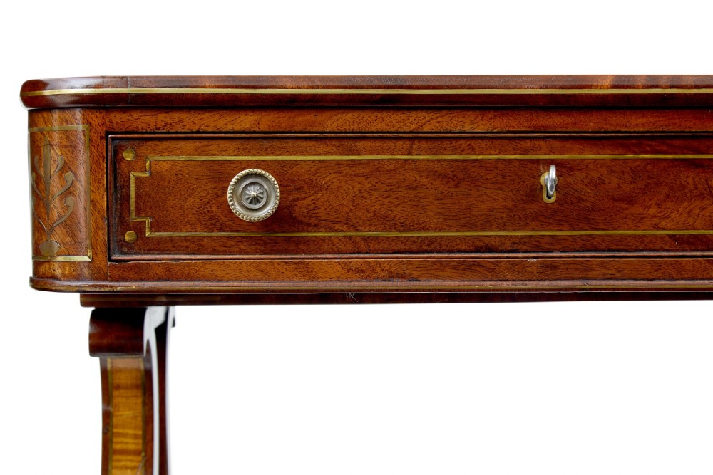 A 19th-century Regency writing desk featuring brass inlay, two frieze drawers, lyre-shaped end supports, and brass paw feet on castors. View VI