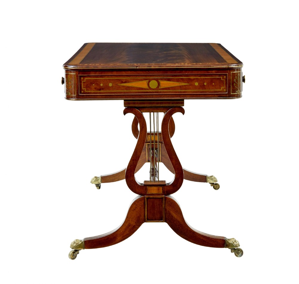 A 19th-century Regency writing desk featuring brass inlay, two frieze drawers, lyre-shaped end supports, and brass paw feet on castors. View VII