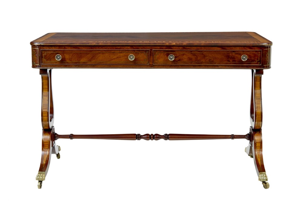 A 19th-century Regency writing desk featuring brass inlay, two frieze drawers, lyre-shaped end supports, and brass paw feet on castors. View IX