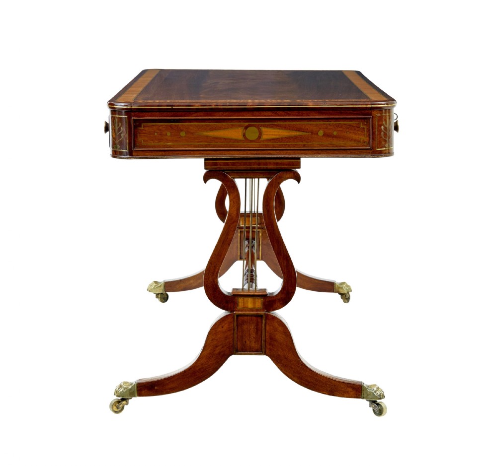 A 19th-century Regency writing desk featuring brass inlay, two frieze drawers, lyre-shaped end supports, and brass paw feet on castors. View X
