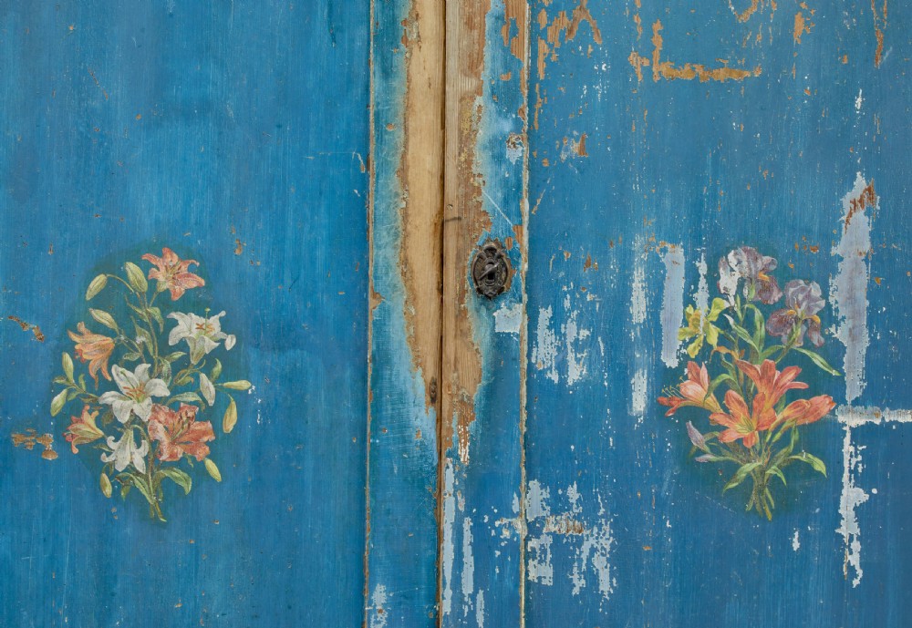 A mid-19th-century Scandinavian pine cupboard featuring distressed blue paint, two panelled doors with painted floral motifs, and short block feet. View VII