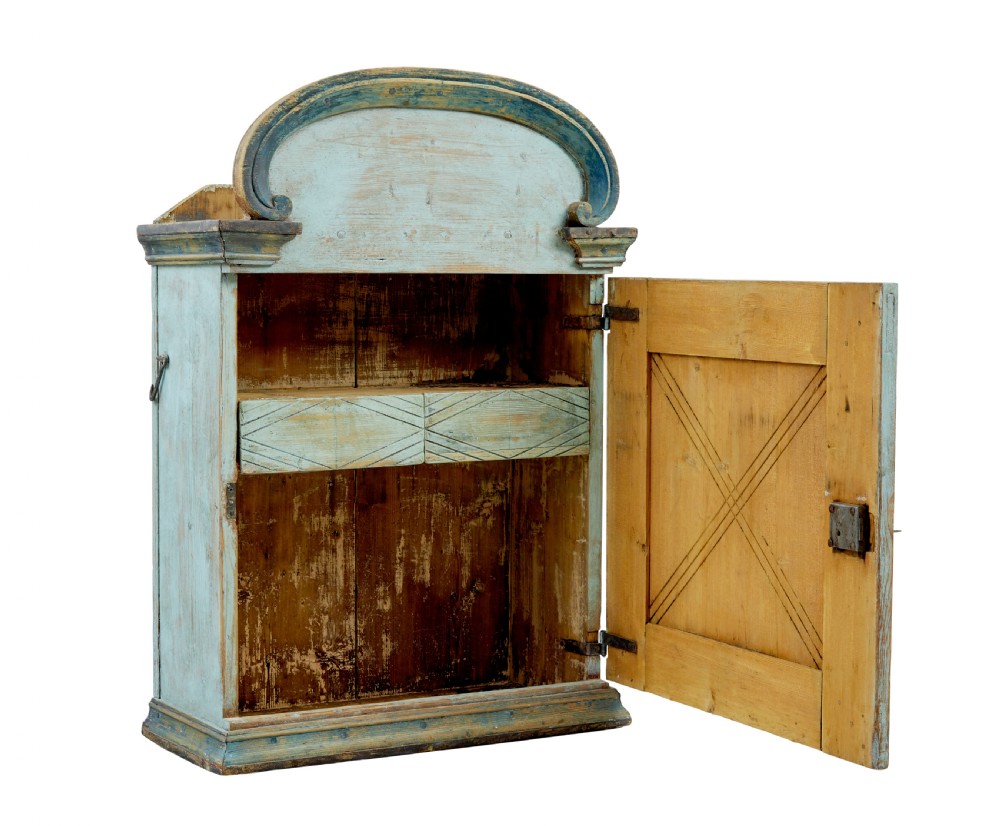 A 19th-century Finnish painted pine wall cupboard featuring weathered light blue paint, an arched pediment crest, and a door panel carved with a diamond pattern. View II