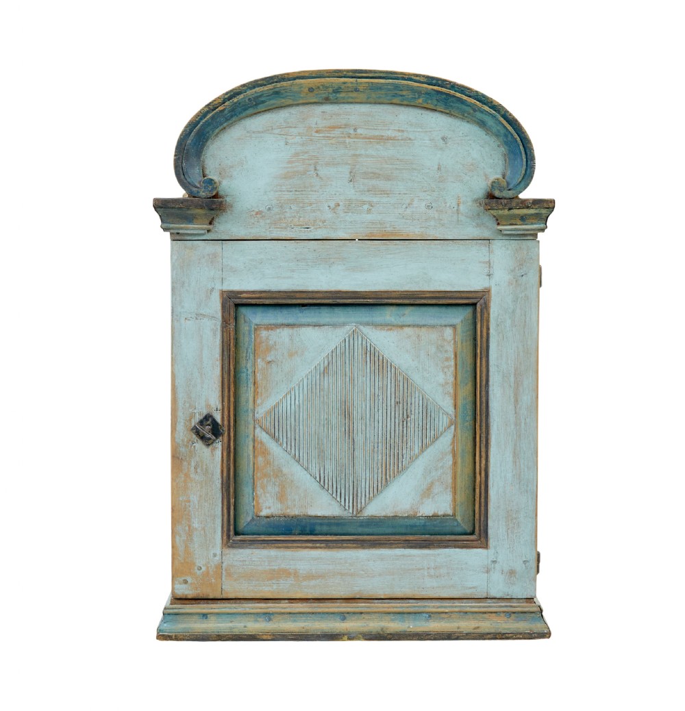 A 19th-century Finnish painted pine wall cupboard featuring weathered light blue paint, an arched pediment crest, and a door panel carved with a diamond pattern. View III