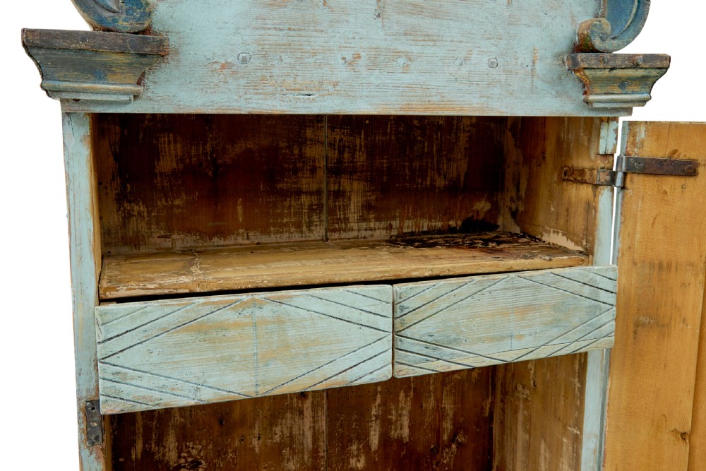A 19th-century Finnish painted pine wall cupboard featuring weathered light blue paint, an arched pediment crest, and a door panel carved with a diamond pattern. View IX