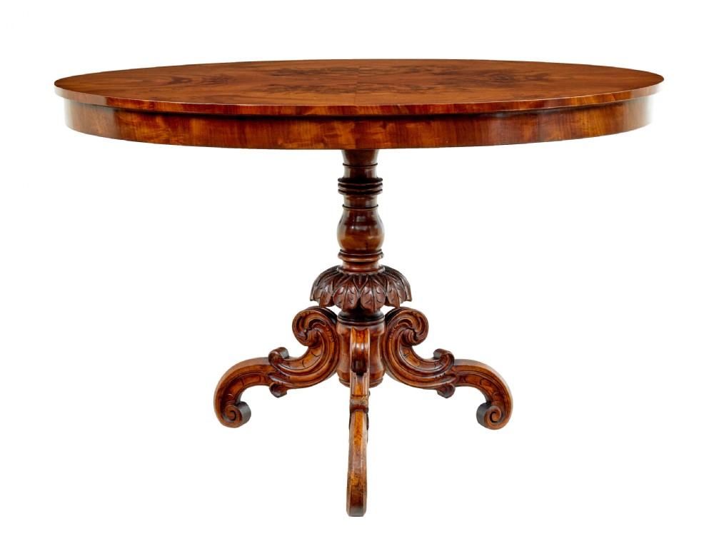 A 19th-century oval wood centre table featuring a figured veneer top, a turned central stem with acanthus leaf carving, and three scroll tripod legs.