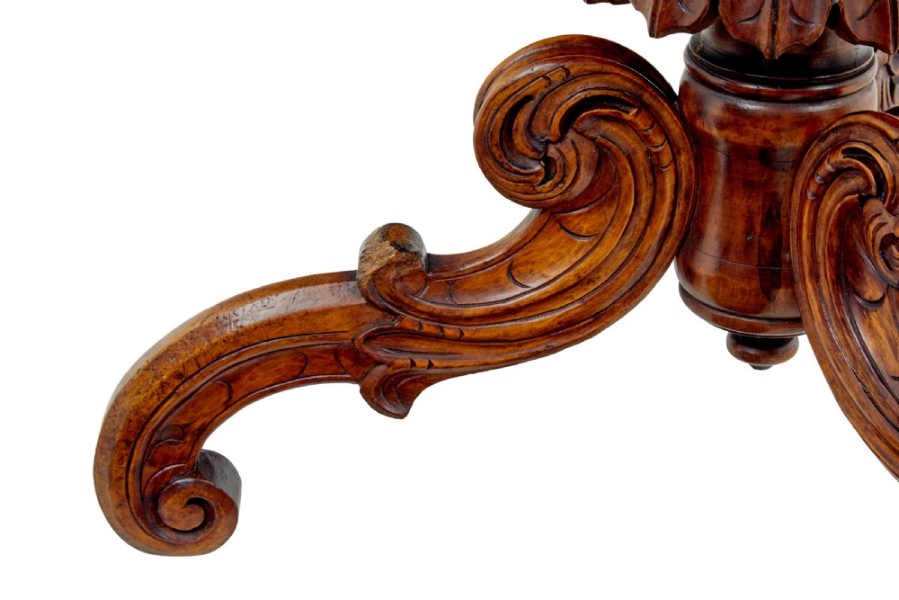 A 19th-century oval wood centre table featuring a figured veneer top, a turned central stem with acanthus leaf carving, and three scroll tripod legs. View VI