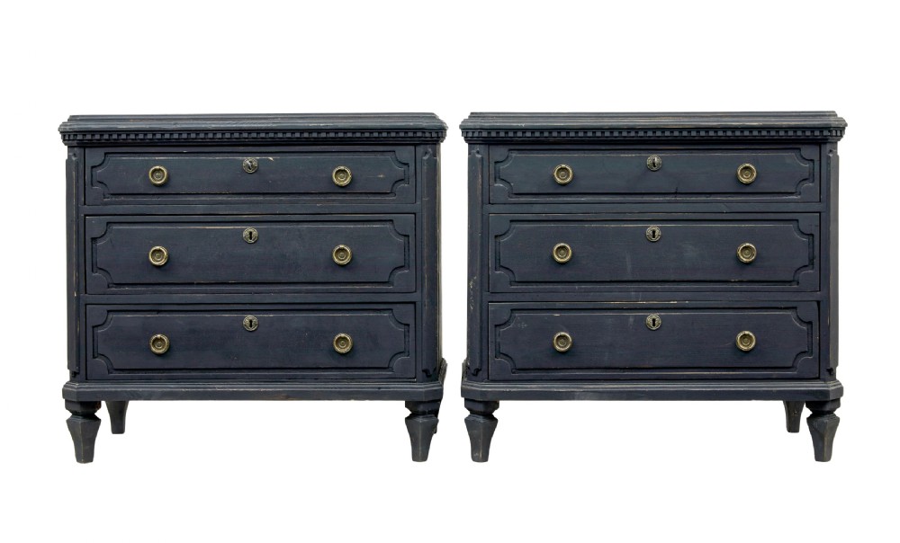 A matching pair of 19th-century Swedish black painted pine commodes, each featuring three drawers with moulded geometric panel fronts and brass drop handles.