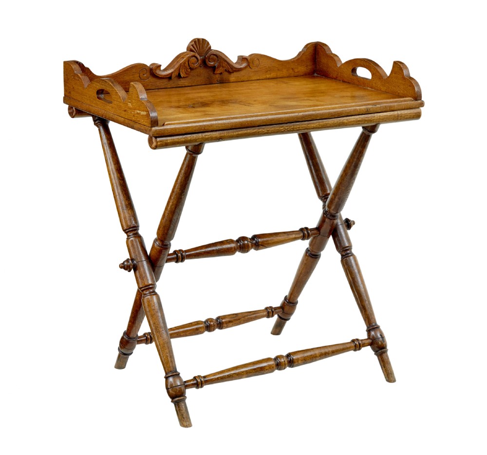 A 19th-century solid oak butler tray with carved gallery handles resting on a folding x-frame stand with turned spindles.