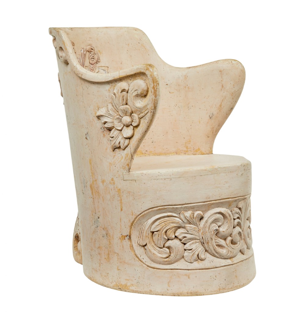 An antique cream-painted dugout armchair carved from a single timber section with relief floral scrollwork and hand-painted figures on the backrest.