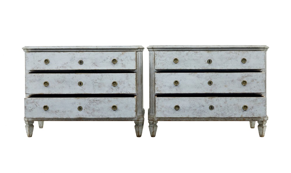 A pair of 19th-century Gustavian style painted chests of drawers with three drawers each, brass pulls, fluted side columns, and distressed pale grey paint. View II