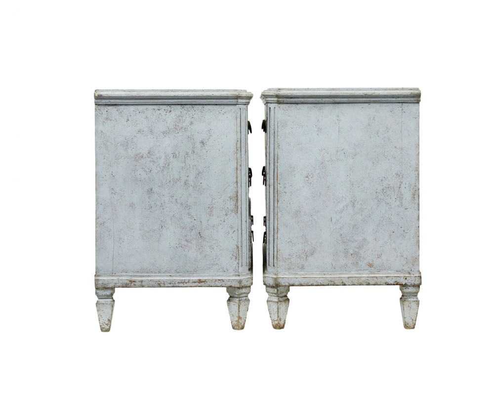 A pair of 19th-century Gustavian style painted chests of drawers with three drawers each, brass pulls, fluted side columns, and distressed pale grey paint. View V